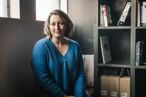 Portrait of Amanda Whitley wearing a blue shirt, sitting by a bookshelf.