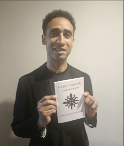 Andrew Geoffrey Kwabena Moss standing against a grey background holding a book.