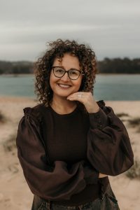 Portrait of Gabbie Stroud standing on a beach, with her left hand touching her chin.
