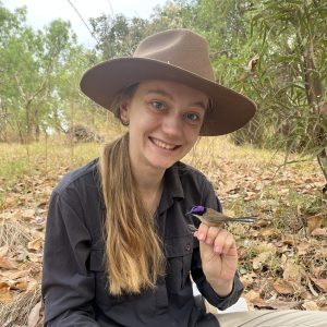 Headshot of Jennifer Evans wearing a sun hat, with a purple-crowned fairy wren perched on her hand.
