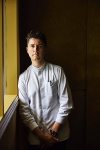 Josh Niland leaning against a yellow window frame, looking pensive.