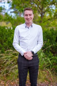 Outdoor portrait of Joshua Black smiling in front of a green garden