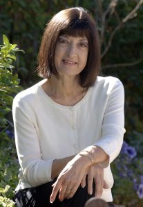 An outdoor portrait of Niki Savva sitting in front of a flower bush.