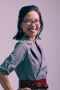 Headshot of Qin Qin smiling, against a grey background.