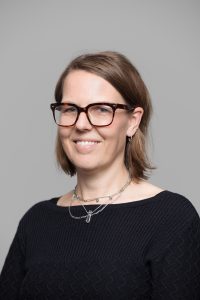 A headshot of Sally Pryor smiling against a solid grey background.