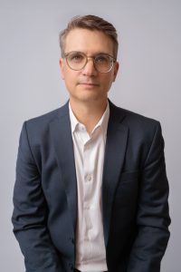 A portrait of Stephen Young against a grey background.