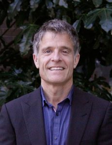 A headshot of Paul Strangio against some dark foliage.