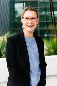 Outdoor headshot of Adele Webb smiling at the camera with plants in the background.
