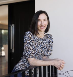 Interior portrait of Catherine Meatheringham leaning against a metal railing and smiling at the camera.