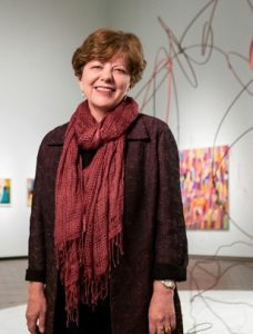 Portrait of Deborah Hart in an art gallery with sculpture and paintings in the background.