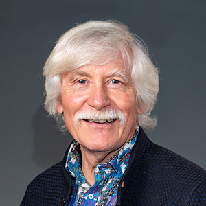 Studio portrait of Hans Bachor smiling at the camera against a plain grey background.