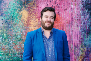Portrait of Michael Williams against a background of colourful splattered paint.