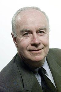 Headshot of Paul Kelly in a business suit, smiling at the camera against a plain white background