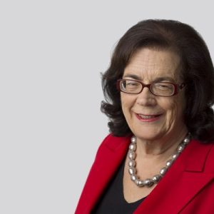 Studio portrait of Michelle Grattan smiling at the camera with a plain light grey background.